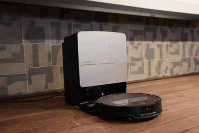 A black robot vacuum approaches its charging station, which is a tall silver and black device.