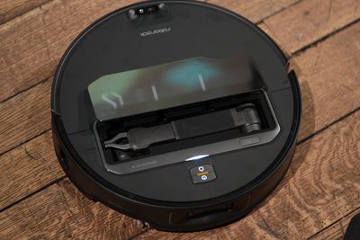 A black robot vacuum on a wooden floor. You can see a folded robotic arm in the center of the robot.